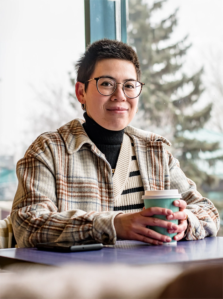 Non-binary person holding a coffee posing for camera